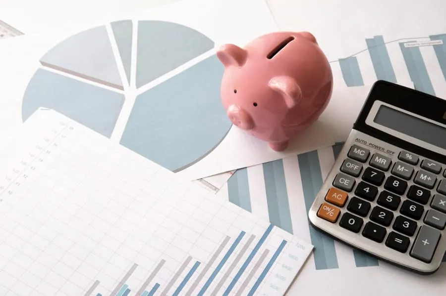 A piggy bank, a calculator and printed charts on a desk
